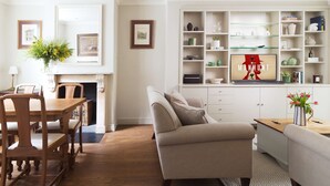 A living room with a fireplace, a sofa, a dining table with chairs, and a bookshelf. - Kings Road 3 bed House Chelsea (London)