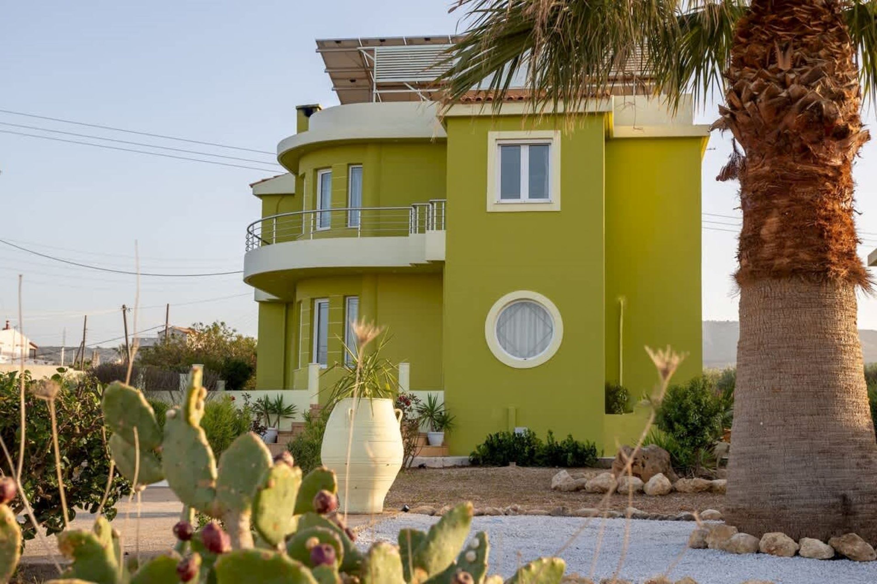Um edifício de vários andares com fachada verde, uma varanda e uma palmeira em primeiro plano.