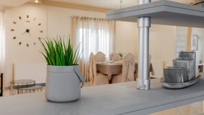 A modern kitchen with a white textured pot on the counter, a clock on the wall, and a dining area in the background. - Villa Amare - Heraklion Private Garden Retreat (Hersonissos)