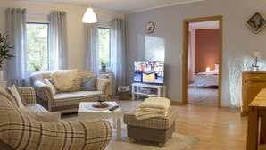 A living room with a sofa, armchair, and ottoman, a TV, a dining table, and a wooden cabinet. - Apartment, Bad Bodenteich (Bad Bodenteich)