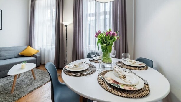 Un comedor con una mesa redonda dispuesta para cuatro personas, un jarrón de flores y una lámpara moderna.