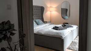 A bedroom with a bed, a bedside lamp, a mirror, and a grey upholstered headboard. - Lovely Family Suite (Apart534), Lovely family suite: luxurious modern apartment with private garden (Prague)