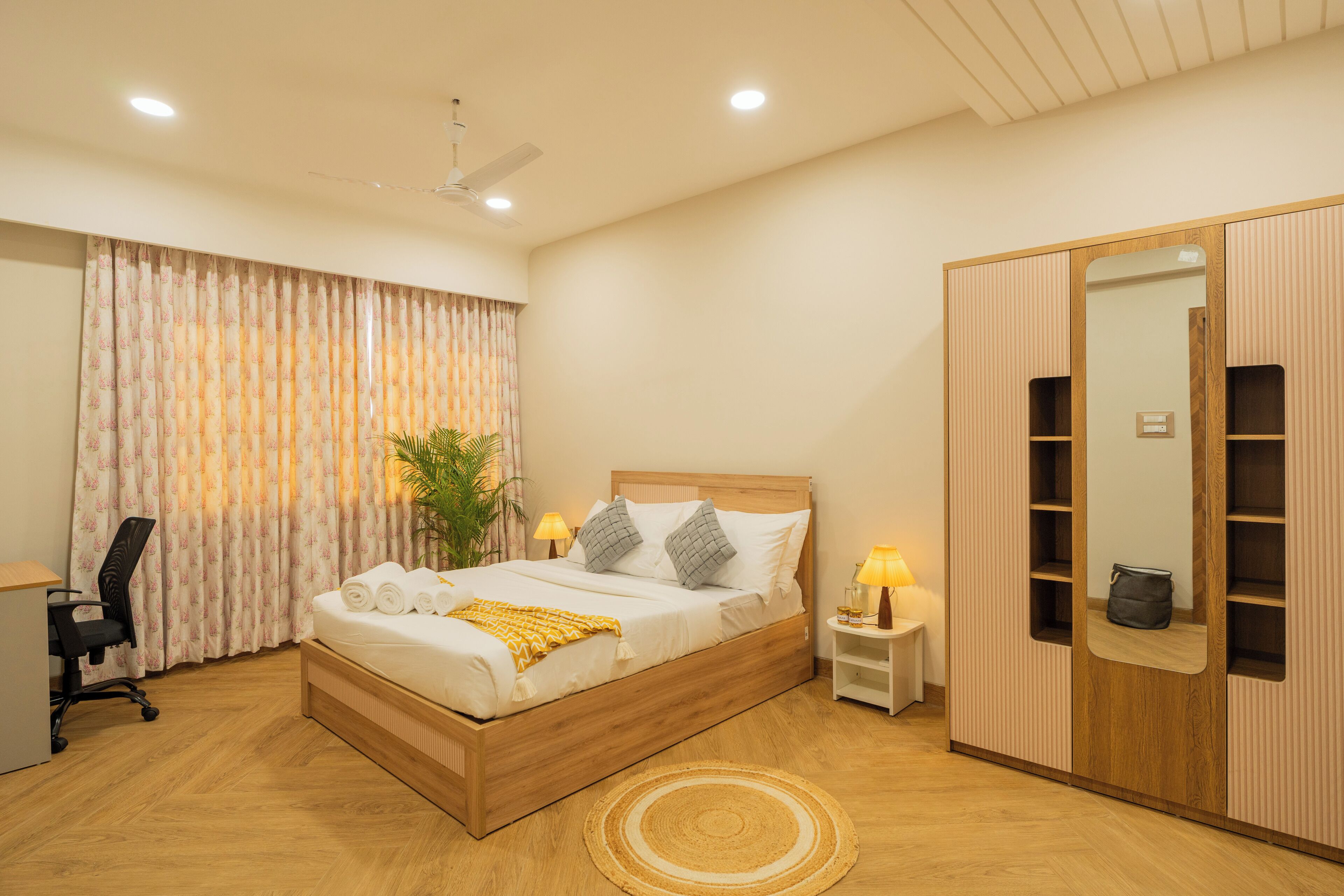 A neatly arranged bedroom with a wooden bed, bedside lamps, a desk, and a wardrobe with a mirror.