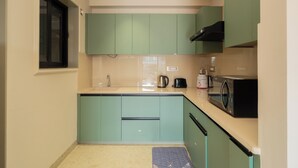 Cocina compacta con armarios verde azulado, un lavamanos, un hervidor, un tostador y un microondas.
