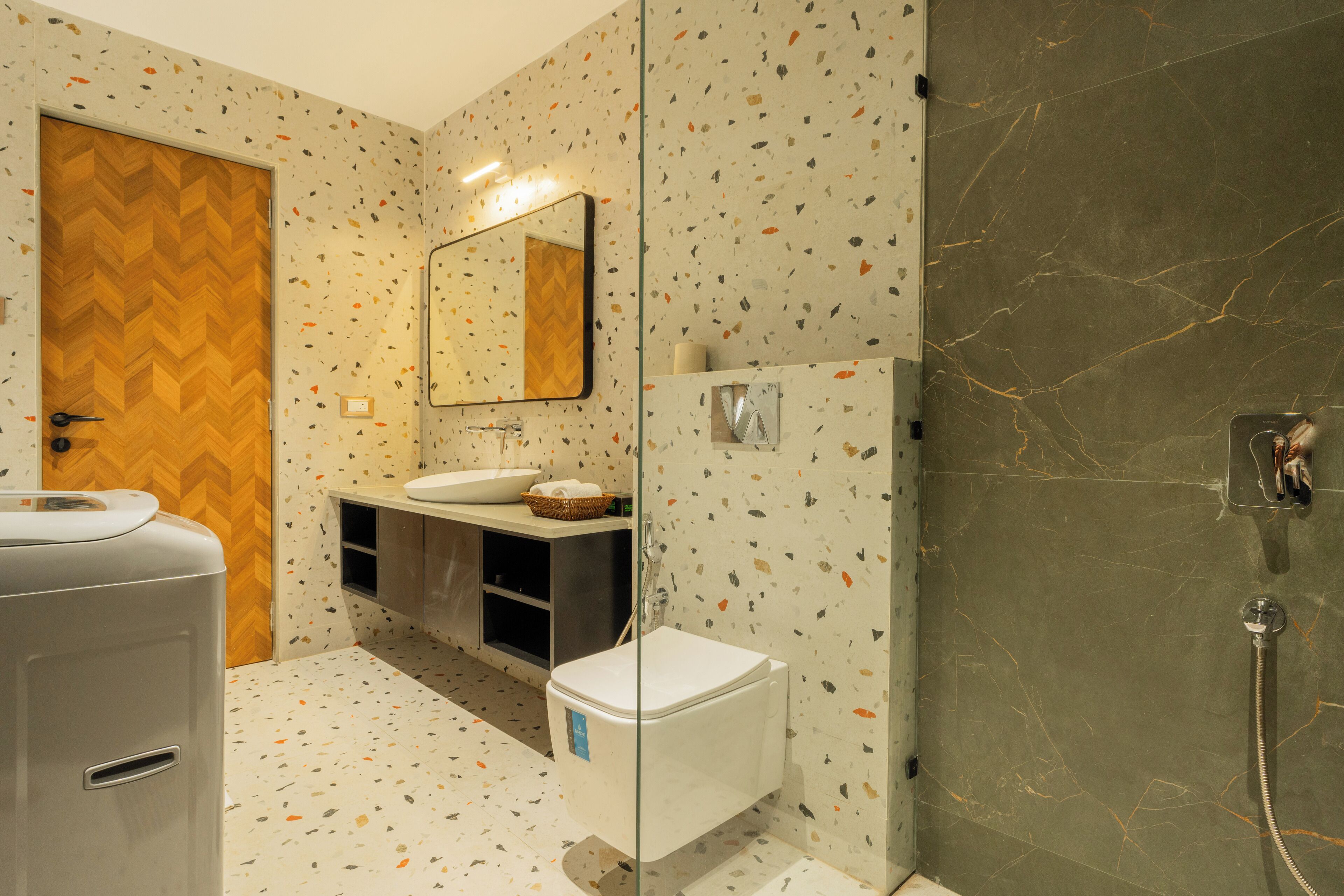 A modern bathroom with a herringbone wood door, a glass shower enclosure, and a white toilet.