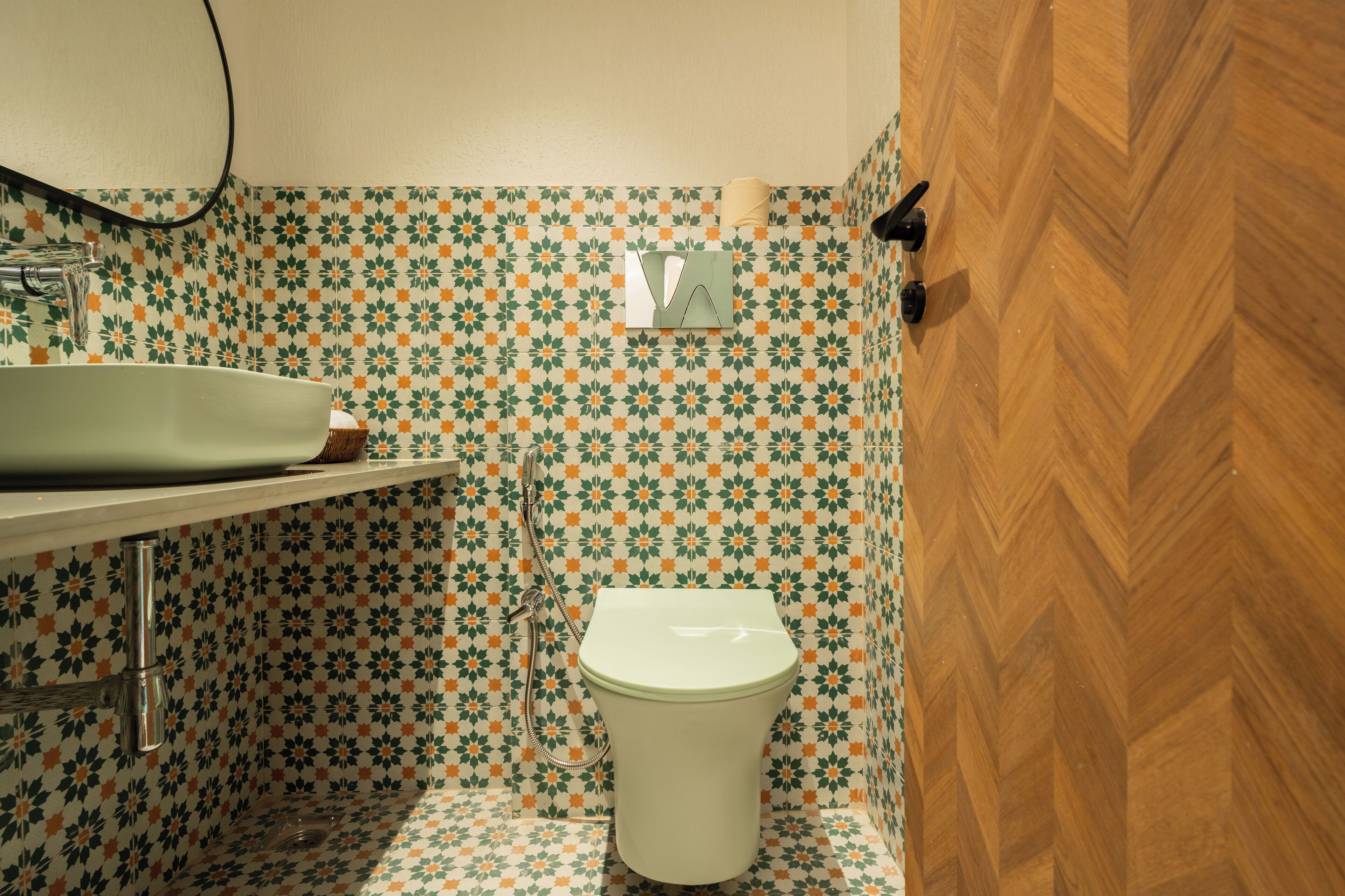 A bathroom with a patterned tile wall, a white toilet, a sink with a mirror, and a wooden door.