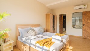 Un dormitorio moderno con una cama de madera, una mesita de noche, una planta en maceta y vista al baño por una puerta abierta.