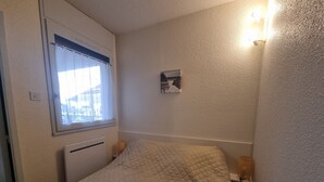 Ein Schlafzimmer mit einem Bett, einem Fenster mit Vorhängen, einem Wandbild und einer Wandleuchte.