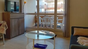 Ein Wohnzimmer mit Fernseher, einem runden Glastisch, einer Couch und einem Balkon mit Stühlen.