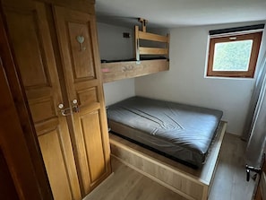 Quarto compacto com beliche, guarda-roupa de madeira e uma pequena janela.