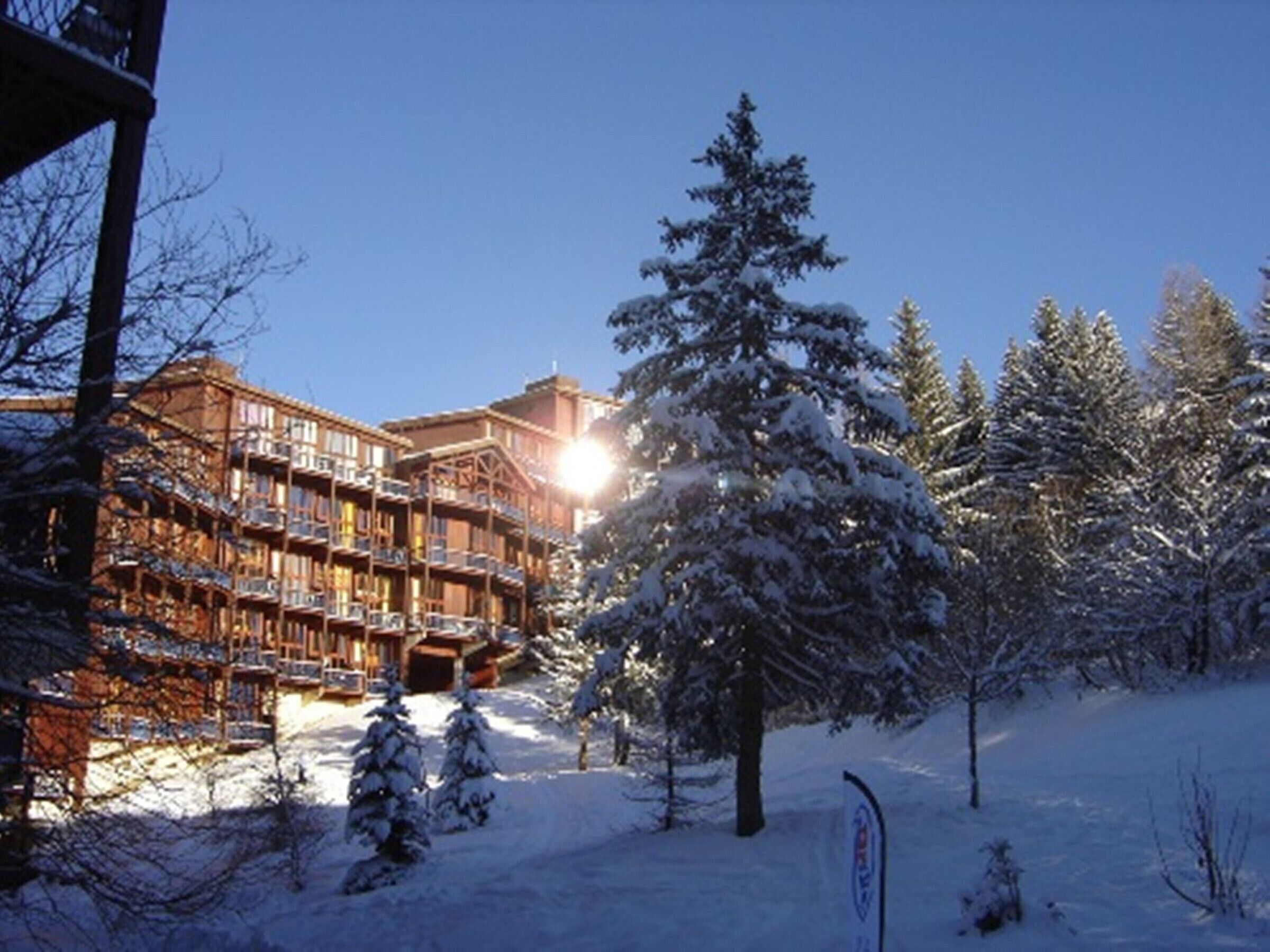 A wooden lodge with multiple balconies and a ski slope in the background.