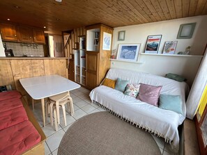 Un interior acogedor con comedor, un sofá con cojines y una cocina con alacenas de madera.
