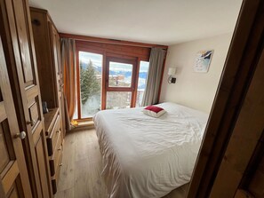 A bedroom with a bed, wooden wardrobe, and a window with a view of mountains.