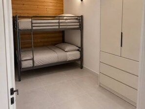Un lit superposé avec une tête de lit en bois, une armoire blanche et un sol carrelé.