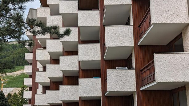 Un edificio a più piani con balconi, ringhiere in legno e una fila di fioriere.