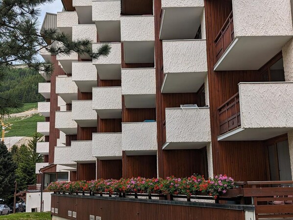 Een meerlaags gebouw met balkons, houten leuningen en een rij bloembakken.