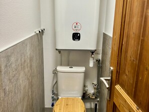 A small bathroom with a toilet, a wooden seat, a white wall, and a wooden door.