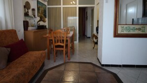 A living room with a sofa, a dining table with chairs, and a kitchen area with cabinets and a refrigerator.