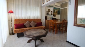 A living room with a sofa, a coffee table, a dining table with chairs, a lamp, and a kitchen area in the background.