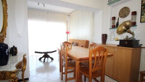 A dining area with a wooden table and chairs, a marble side table, and a cabinet with decorative items.