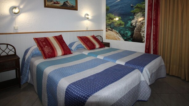 A bedroom with two beds, a painting, and a view of the sea.