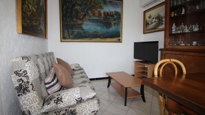 A living room with a sofa, a wooden dining table, a television, and a bookshelf. - 6-Person Beach Apt, Pets Allowed. (Llançà)