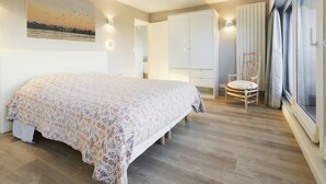 A bedroom with a bed, a chair, a wardrobe, and a large window. - Beautiful apartment in Touquet, sea view balcony, wifi, box included (Le Touquet-Paris-Plage)