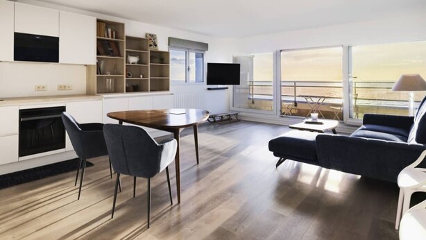 A modern living room with a dining area, a sofa, a TV, and a view of the sea. - Beautiful apartment in Touquet, sea view balcony, wifi, box included (Le Touquet-Paris-Plage)