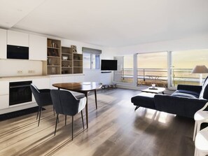 A modern living room with a dining area, a sofa, a TV, and a view of the sea. - Beautiful apartment in Touquet, sea view balcony, wifi, box included (Le Touquet-Paris-Plage)