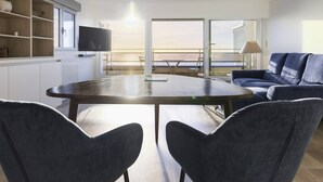 A modern living room with a round table, two chairs, a sofa, a TV, and a view of the sea through large windows. - Beautiful apartment in Touquet, sea view balcony, wifi, box included (Le Touquet-Paris-Plage)