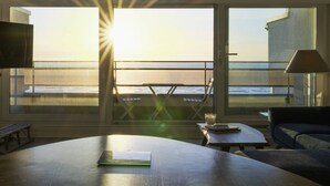 A room with a large window overlooking the sea, a table with a book, a chair, and a lamp. - Beautiful apartment in Touquet, sea view balcony, wifi, box included (Le Touquet-Paris-Plage)