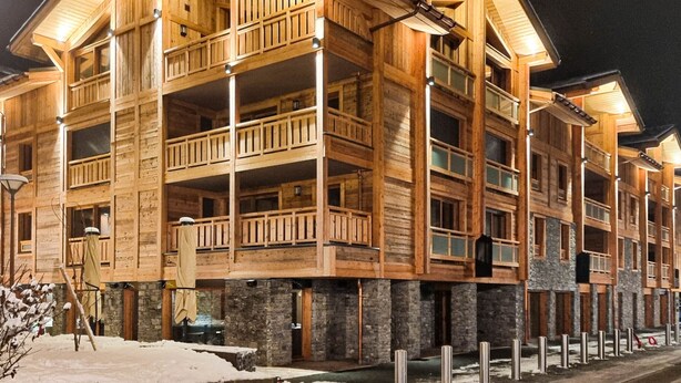 En flervåningsbyggnad i trä med balkonger och stora fönster, troligen ett hotell eller ett semesteranläggning.