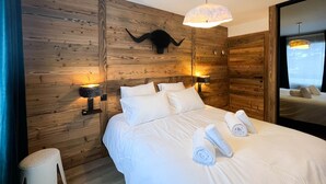 Ett modernt sovrum med en väggpanel av trä, en säng med vita sängkläder, två sänglampor och en stor spegel.