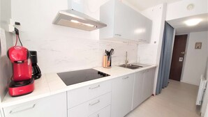 Una cucina moderna con mobili bianchi, un piano cottura a induzione nero, una macchina da caffè rossa e un lavello in acciaio inossidabile.