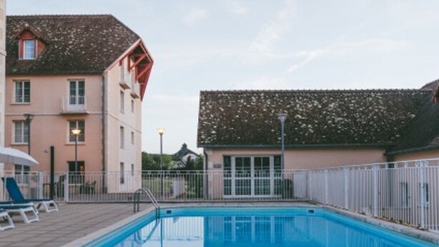 A swimming pool with a white fence, a building with a red roof, and a clear sky. - Renovated apartment near Thermes with pool and Wi-Fi (La Roche-Posay)
