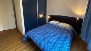 A bedroom with a bed, a wardrobe, and a nightstand with a lamp. - Renovated apartment near Thermes with pool and Wi-Fi (La Roche-Posay)