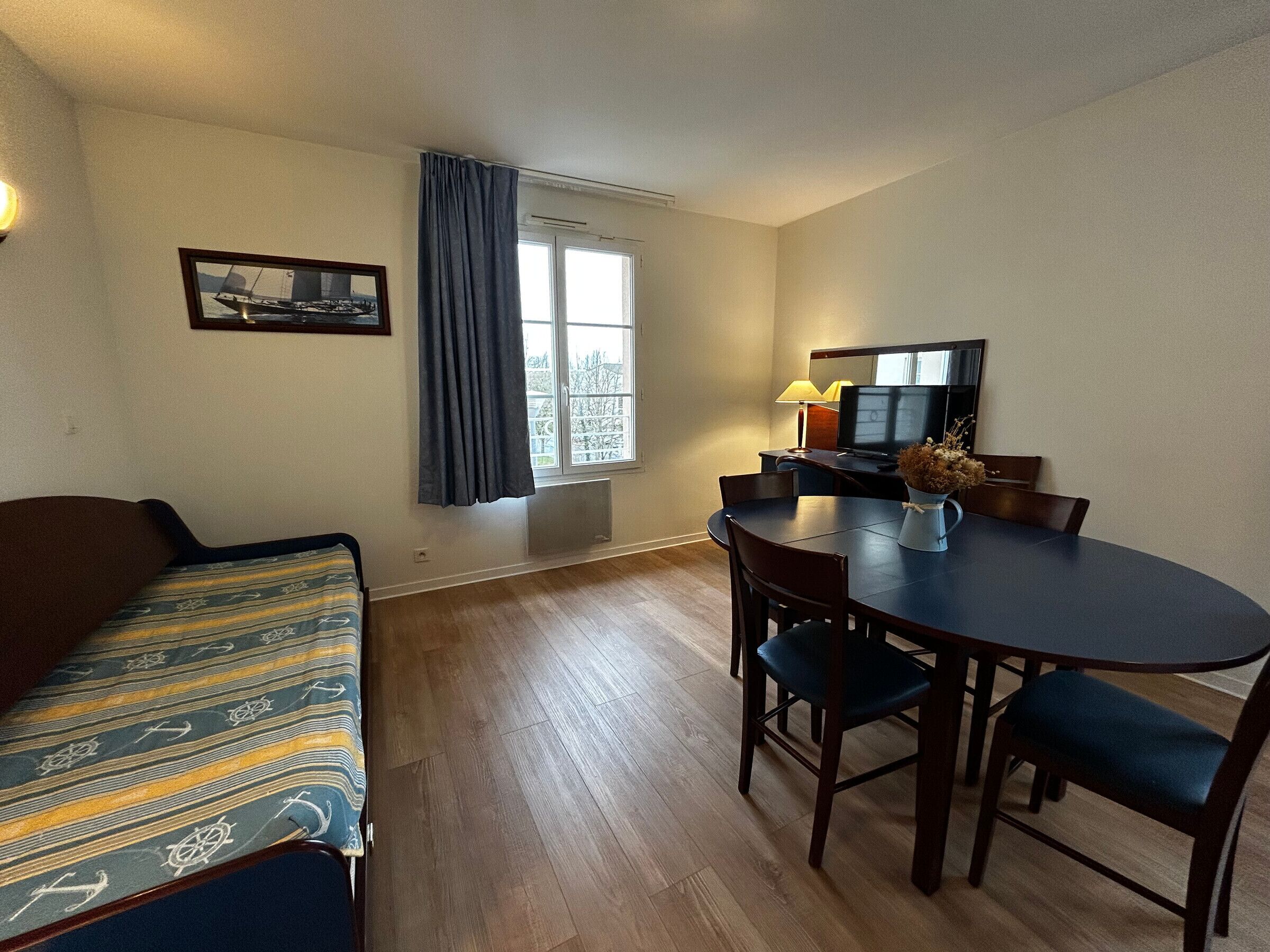 Een kamer met een bank, een eettafel met stoelen, een televisie en een raam met gordijnen.