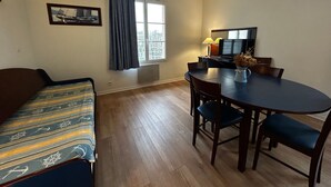 A room with a sofa, a dining table with chairs, a television, and a window with curtains. - Renovated apartment near Thermes with pool and Wi-Fi (La Roche-Posay)