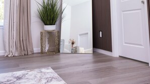 Un couloir moderne avec un plancher en bois, un tapis beige, une plante en pot, un miroir et une porte.