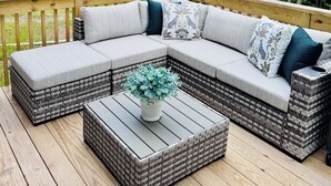 Une terrasse avec un canapé d’angle en osier, une table basse et une plante en pot.