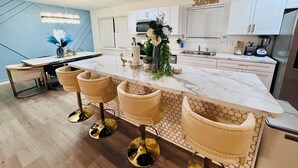 Une cuisine moderne avec un plan de travail en marbre, un îlot central doté de tabourets et une enseigne « Cuisine » au-dessus des placards.