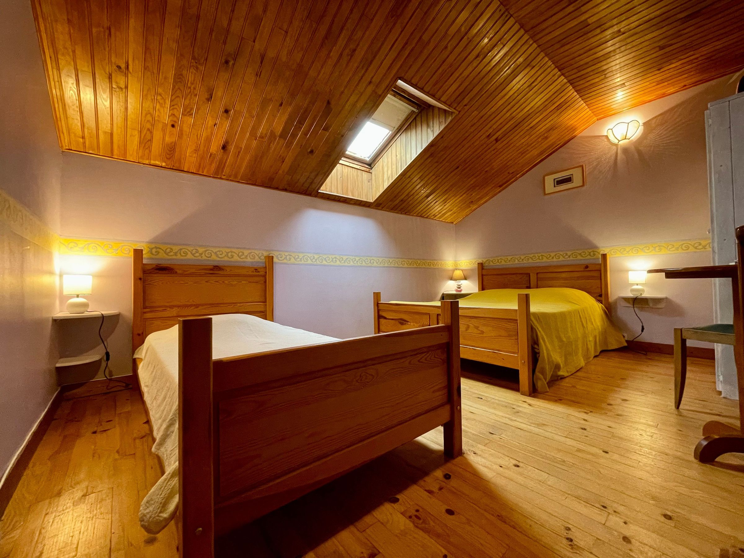 Ein Schlafzimmer mit zwei hölzernen Betten, einem Oberlicht und Nachttischlampen.
