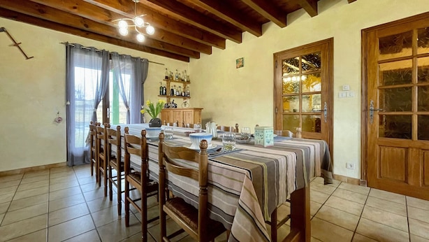 A dining room with a long table set for six, wooden chairs, a chandelier, and a view through a window to the outside. - Lilas Room in Alleyras - Pets allowed, Guest table, Spacious grounds (Alleyras)