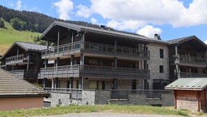 A multi-story hotel with balconies, stone facade, and a mountainous backdrop. - New apartment in Les Gets, 3 bedrooms, mountain view, parking (Les Gets)