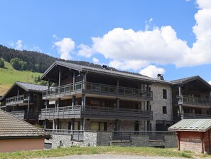 A multi-story hotel with balconies, stone facade, and a mountainous backdrop.