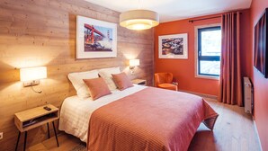 A modern hotel room with a wooden wall, a large bed with a red blanket, two bedside lamps, and a window with curtains. - New apartment in Les Gets, 3 bedrooms, mountain view, parking (Les Gets)