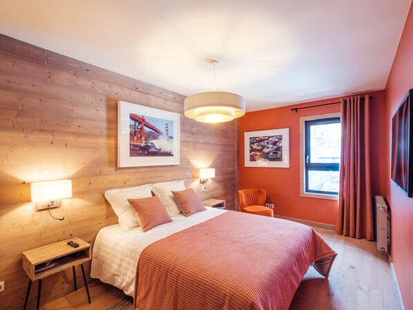 A modern hotel room with a wooden wall, a large bed with a red blanket, two bedside lamps, and a window with curtains.