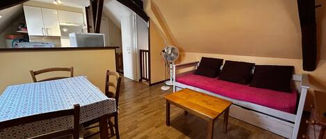 A cozy room with a wooden table, a sofa with a red blanket, and a fan.
