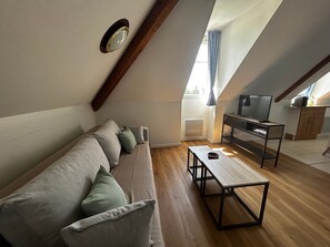 Ein Loft-Zimmer mit einer Couch, einem Tisch, einem Fernseher und einem Fenster mit Vorhängen.
