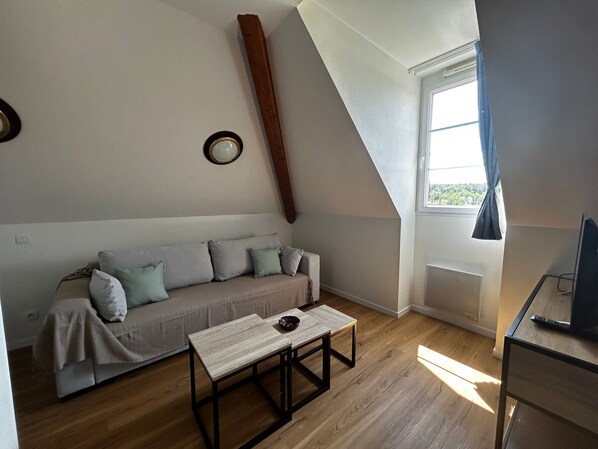 A room with a sloped ceiling, a sofa with cushions, a small table, and a window with curtains.